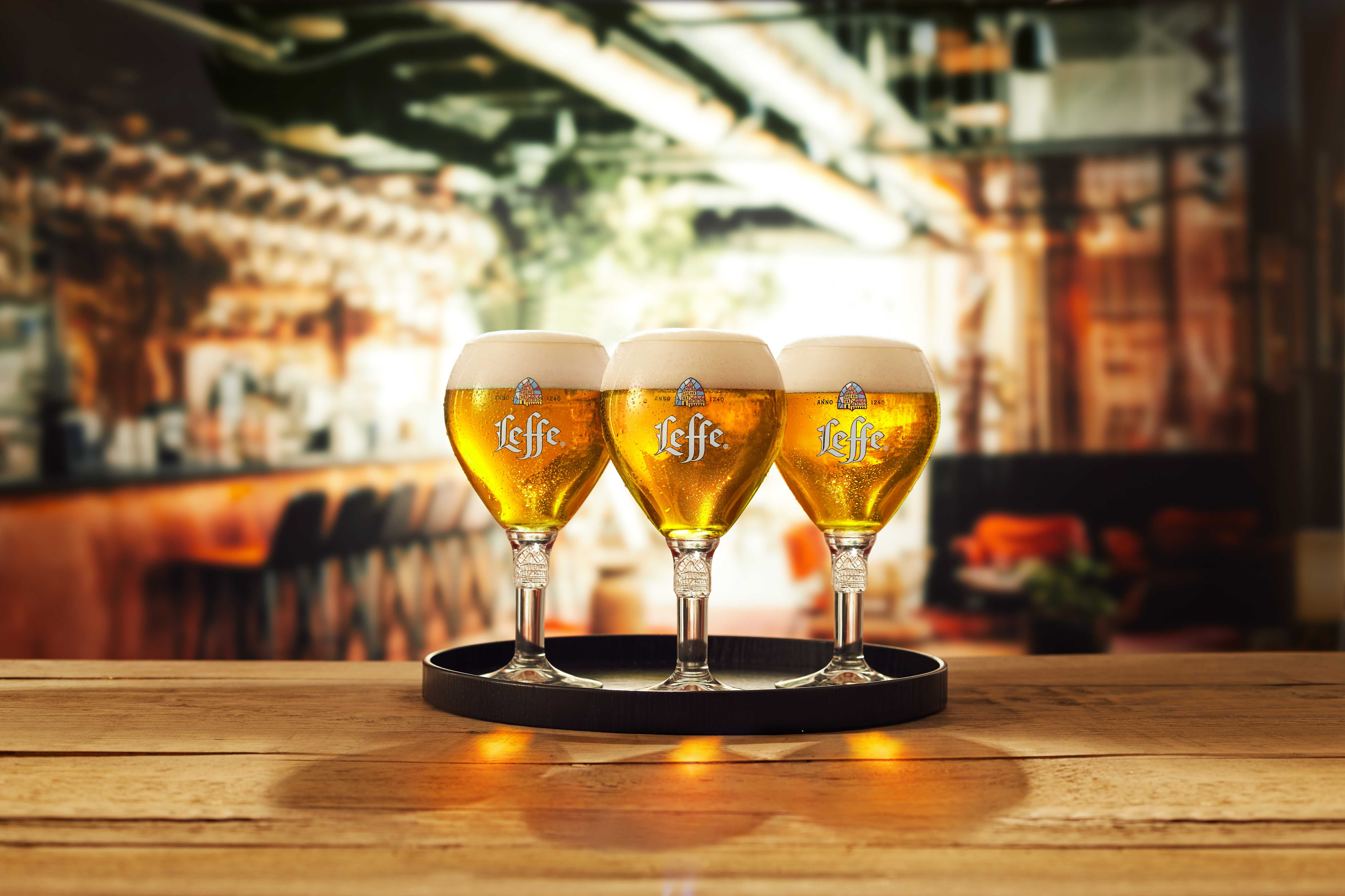 Three Leffe pint glasses with beer in on a tray